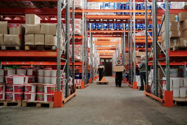 Warehouse interior showing workers handling boxes and organized shelves filled with products.