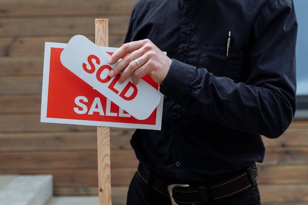 A real estate agent placing a sold sticker over a sale sign, indicating successful property deal.