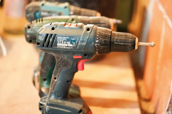 A row of cordless power drills on a wooden workbench, ready for use.