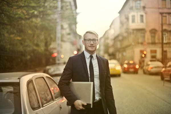 Businessman in a suit holding a laptop on a busy city street. Urban professional life.