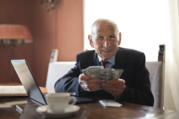 Elderly man smiling while counting cash at a home office setting.