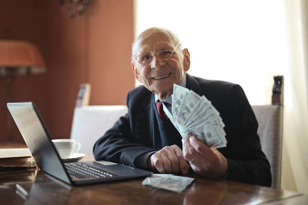 Happy senior businessman showing cash at his desk with a laptop, indoors.