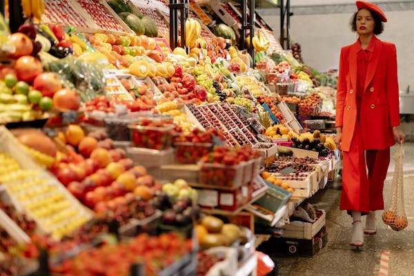 Stylish woman in red outfit shopping for fresh fruits at a bustling market.