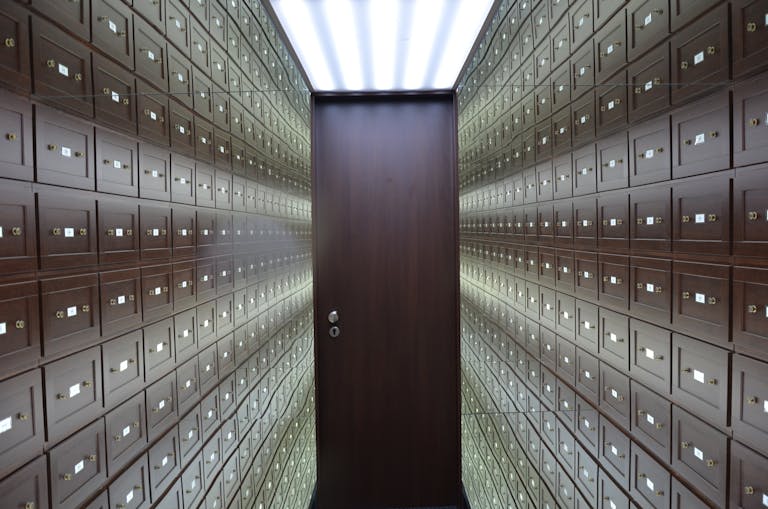 Wooden lockboxes line the walls of a modern, secure vault with a central wooden door.